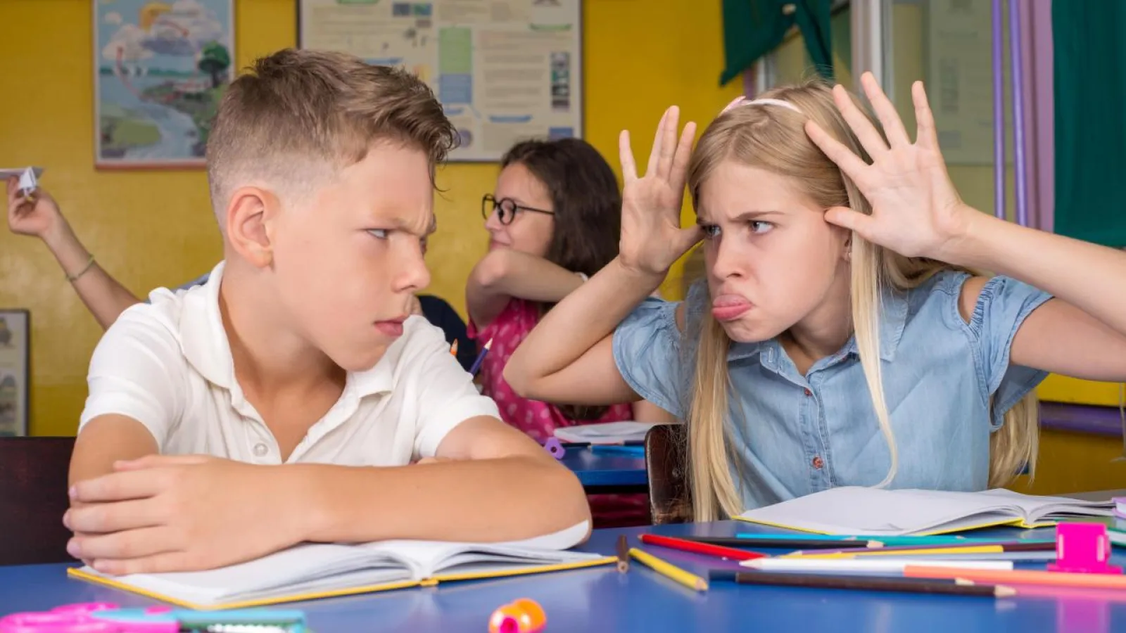 A girl sticks out her tongue and mocks a boy in a school classroom.